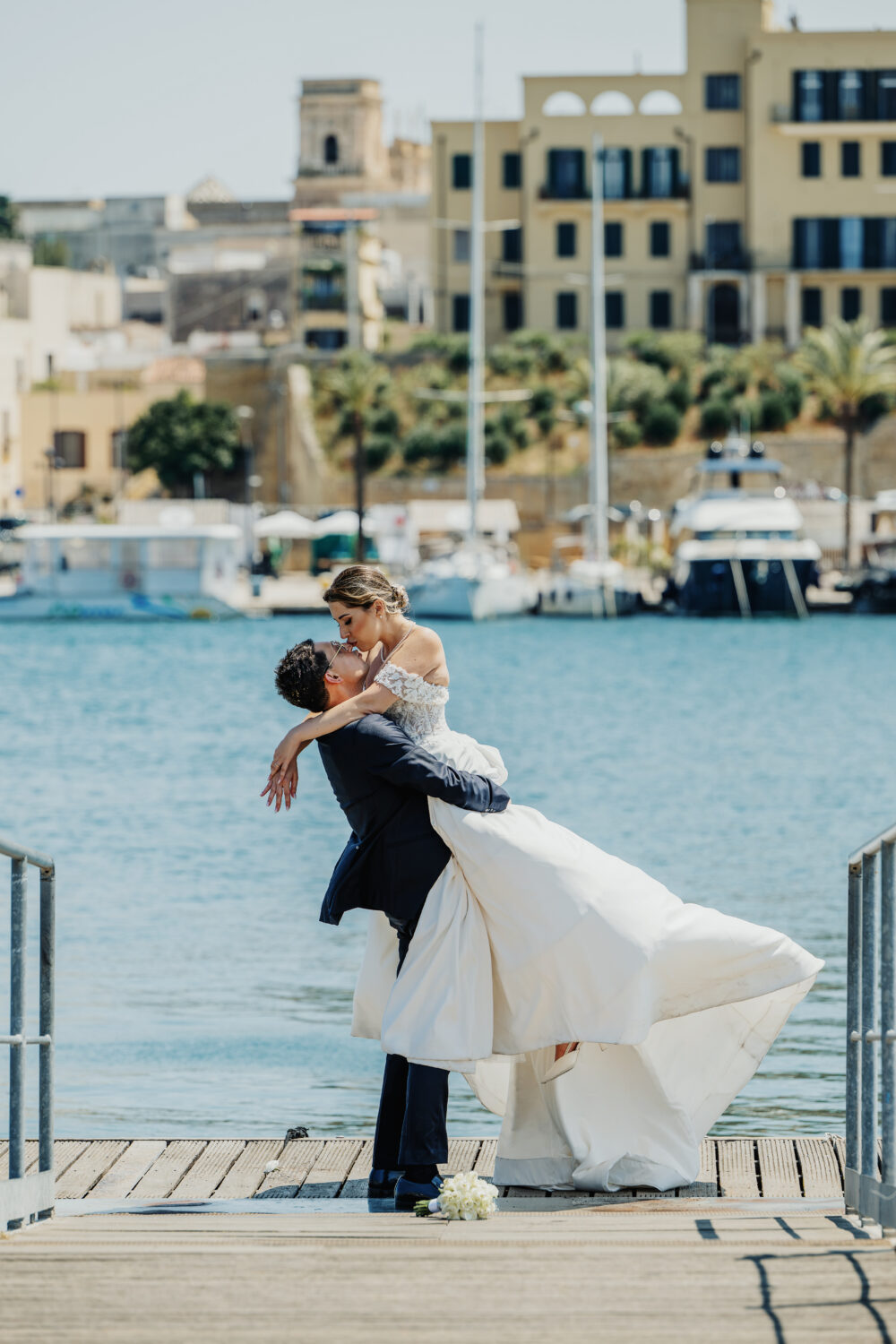 Sposo solleva la sposa sul molo del porto turistico in Puglia