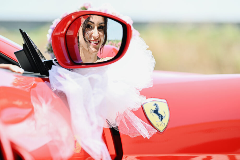 Riflesso sposa nello specchietto di una Ferrari rossa auto da matrimonio